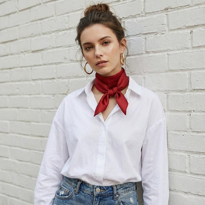 Foulard en soie rouge noué autour du cou d'une femme, avec un haut blanc et un fond de mur en