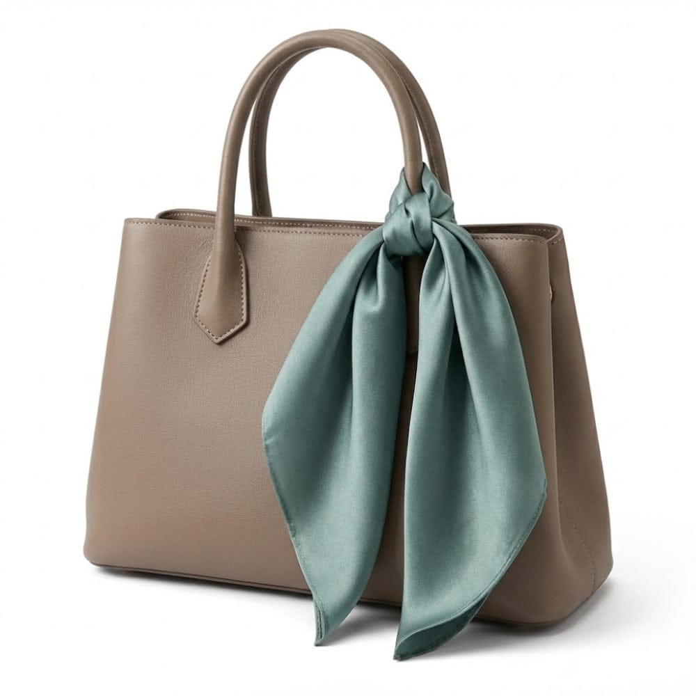 Foulard en soie vert d'eau noué sur un sac à main beige, ajoutant une touche d'élégance intemporelle