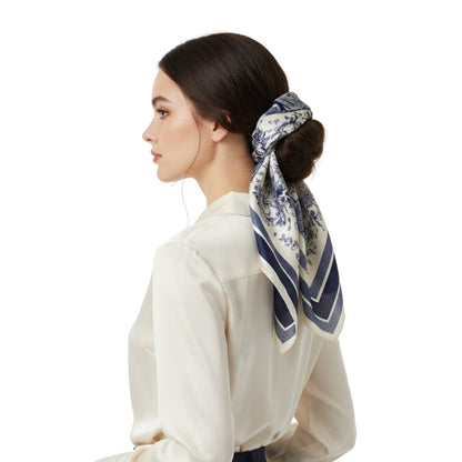 Foulard en soie bleu marine à motifs floraux, noué élégamment dans les cheveux d'une femme en chemise claire