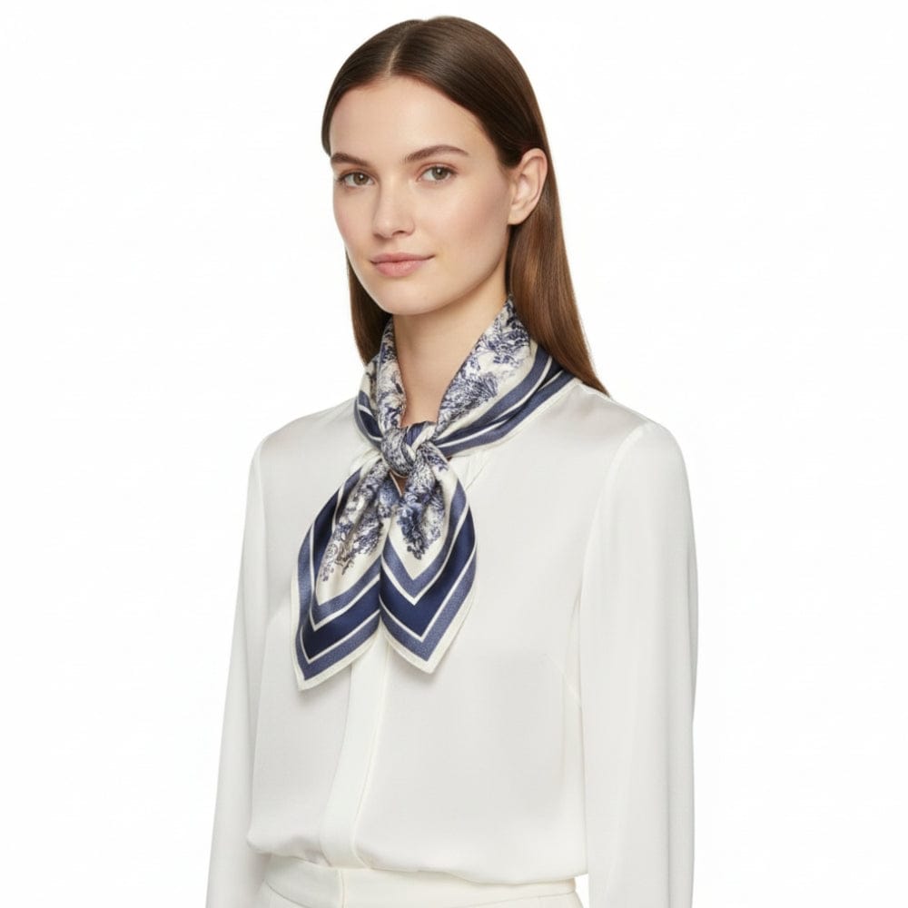 Foulard en soie noué autour du cou, avec des motifs floraux et des rayures bleues sur fond blanc, porté par