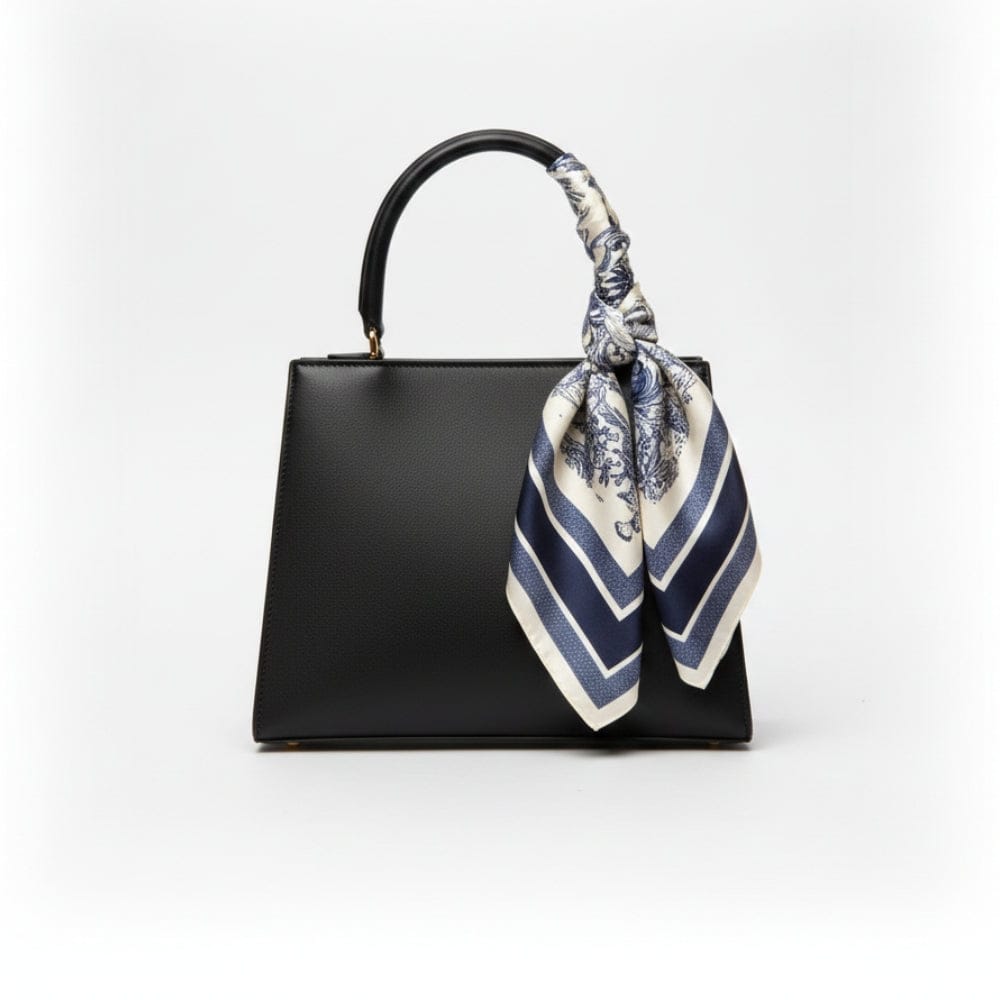 Foulard en satin noué sur un sac noir, avec motifs floraux bleus et rayures blanches, ajoutant une touche élégante