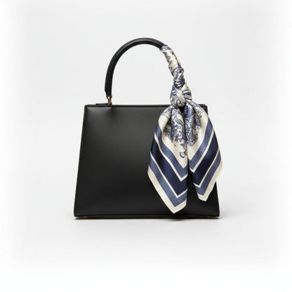 Foulard en satin noué sur un sac noir, avec motifs floraux bleus et rayures blanches, ajoutant une touche élégante
