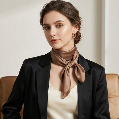 Foulard en soie noué autour du cou d'une femme, couleur beige, porté avec une blouse satinée et un blazer noir