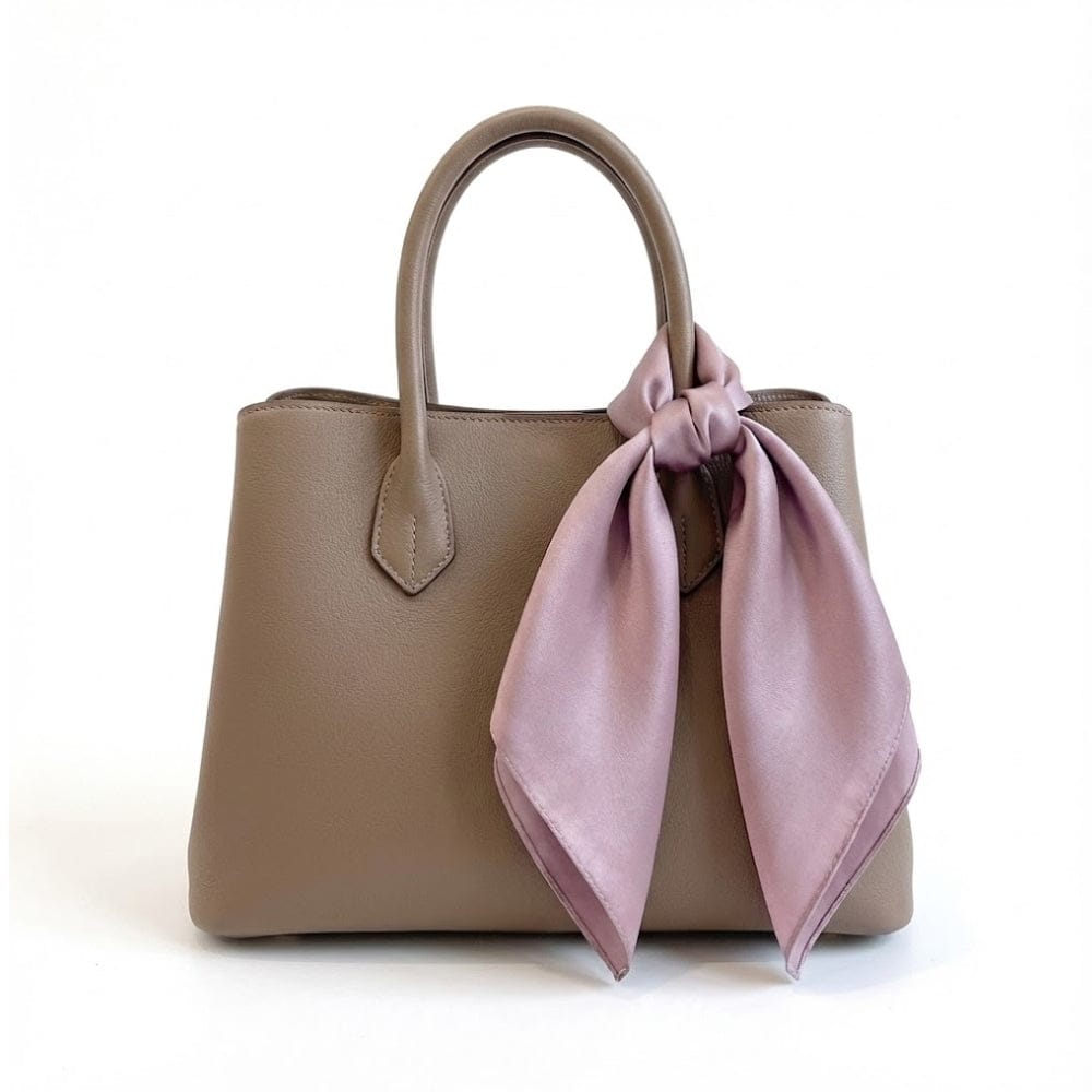 Foulard en satin parme délicat noué sur un sac à main en cuir beige, ajoutant une touche élégante