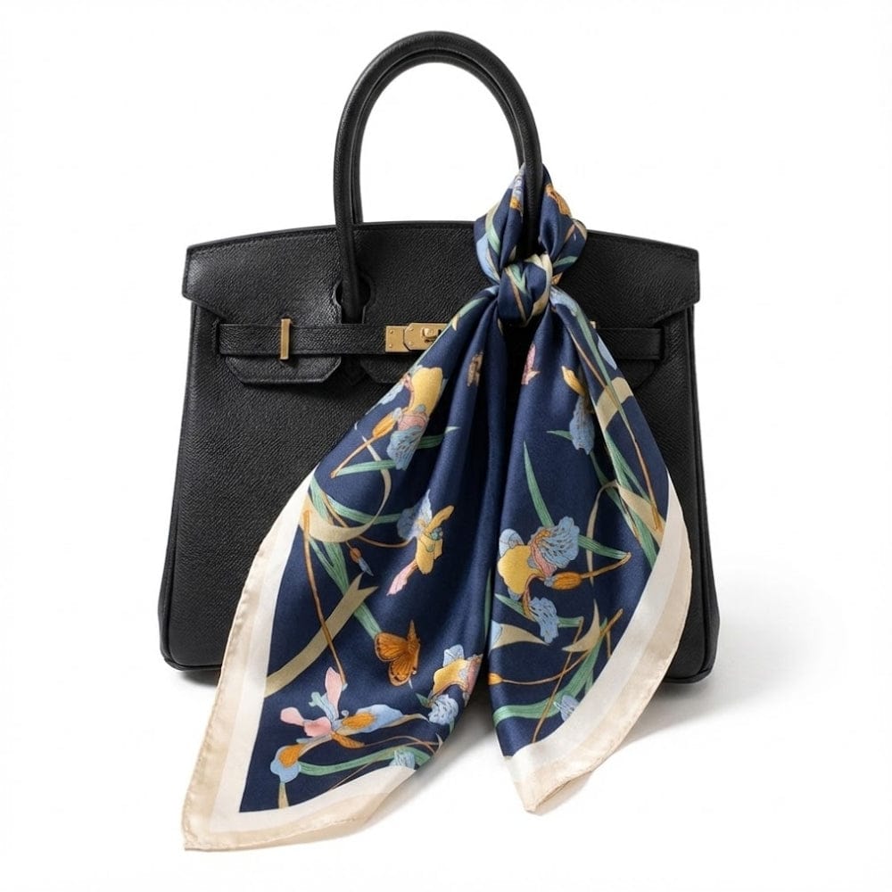 Foulard en satin bleu marine aux motifs floraux colorés, noué sur un sac à main noir élégant