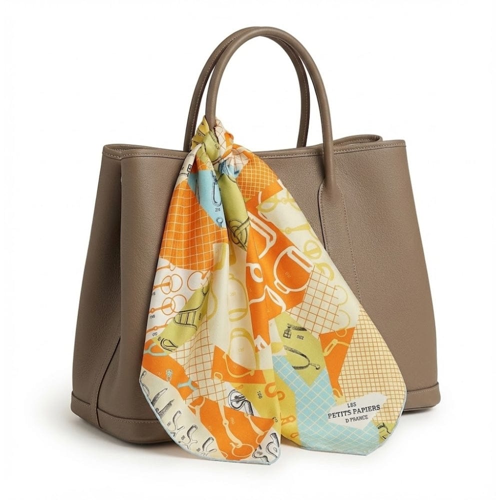 Foulard en soie aux motifs colorés, orange éclatant et jaune, noué sur un sac à main beige élégant