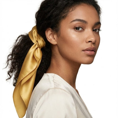 Foulard en soie jaune moutarde noué dans les cheveux d'une femme, sur fond blanc, dégageant une allure sophistiquée