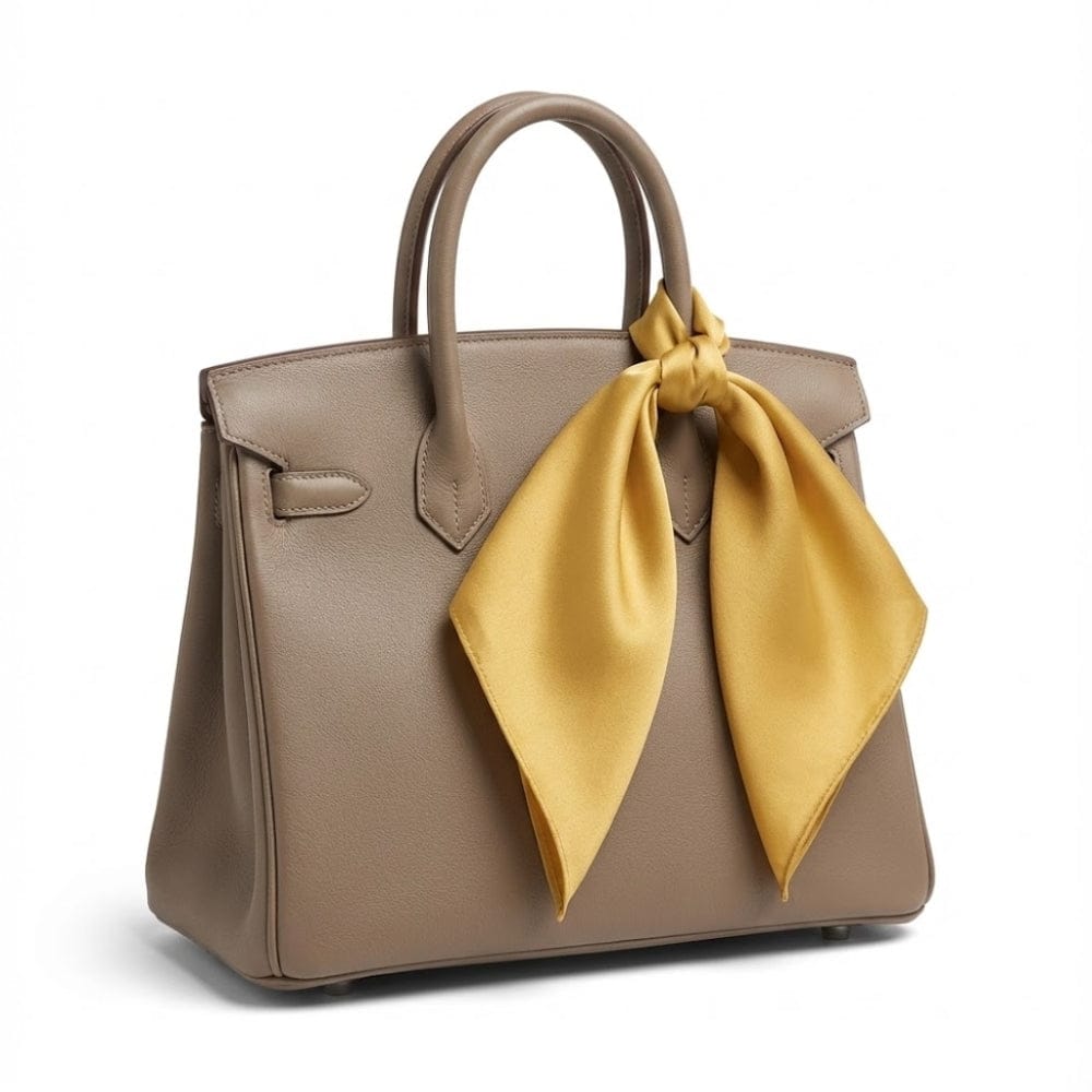 Foulard en soie jaune moutarde noué élégamment sur un sac à main beige, ajoutant une touche sophistiquée