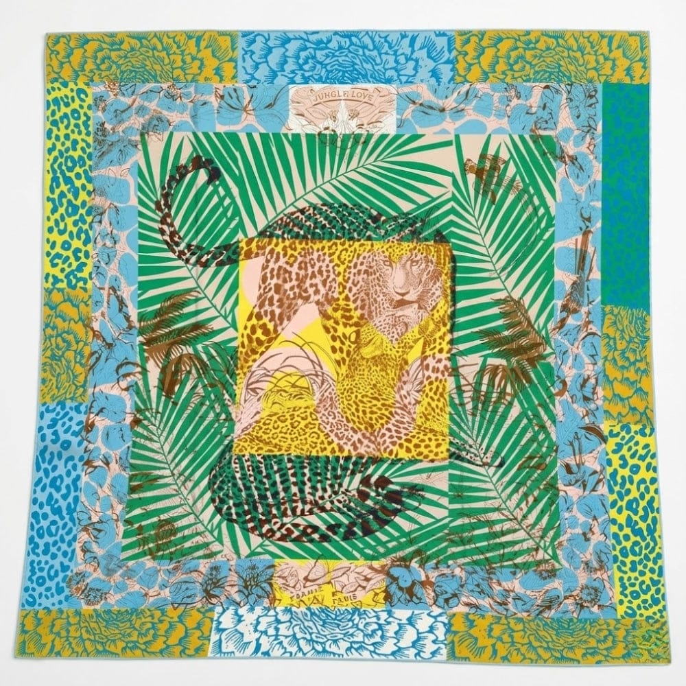 Foulard carré en soie aux motifs léopard colorés, entouré de feuillages verts et floraux, posé sur fond blanc