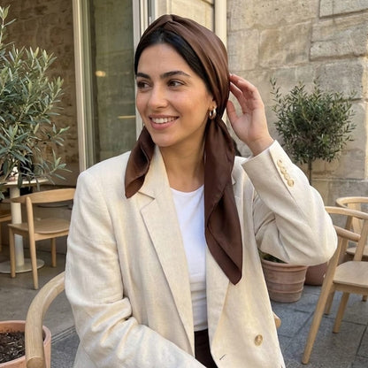 Foulard en satin marron noué sur la tête, porté par une femme souriante dans un café élégant