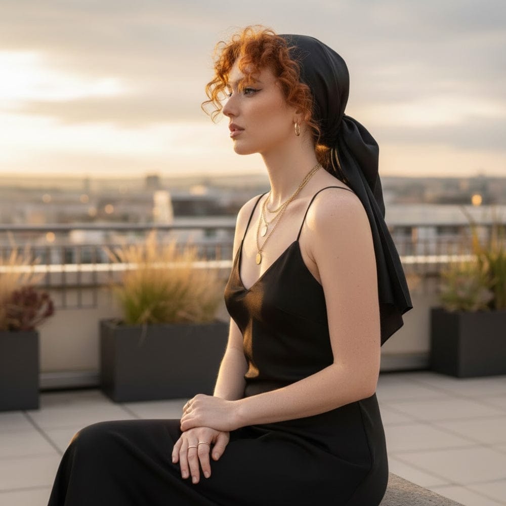 Foulard noir en satin noué sur une femme aux cheveux bouclés, avec un décor urbain en arrière-plan