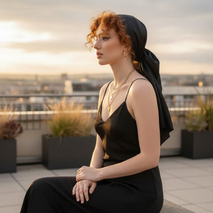 Foulard noir en satin noué sur une femme aux cheveux bouclés, avec un décor urbain en arrière-plan