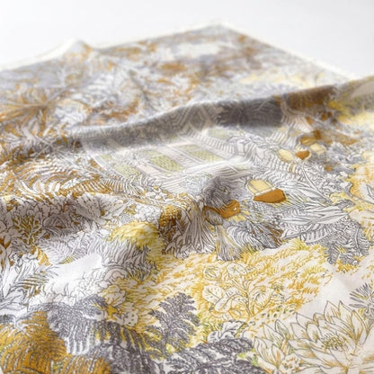 Foulard en soie aux motifs floraux délicats, dominé par des teintes jaunes et grises, posé sur une surface blanche
