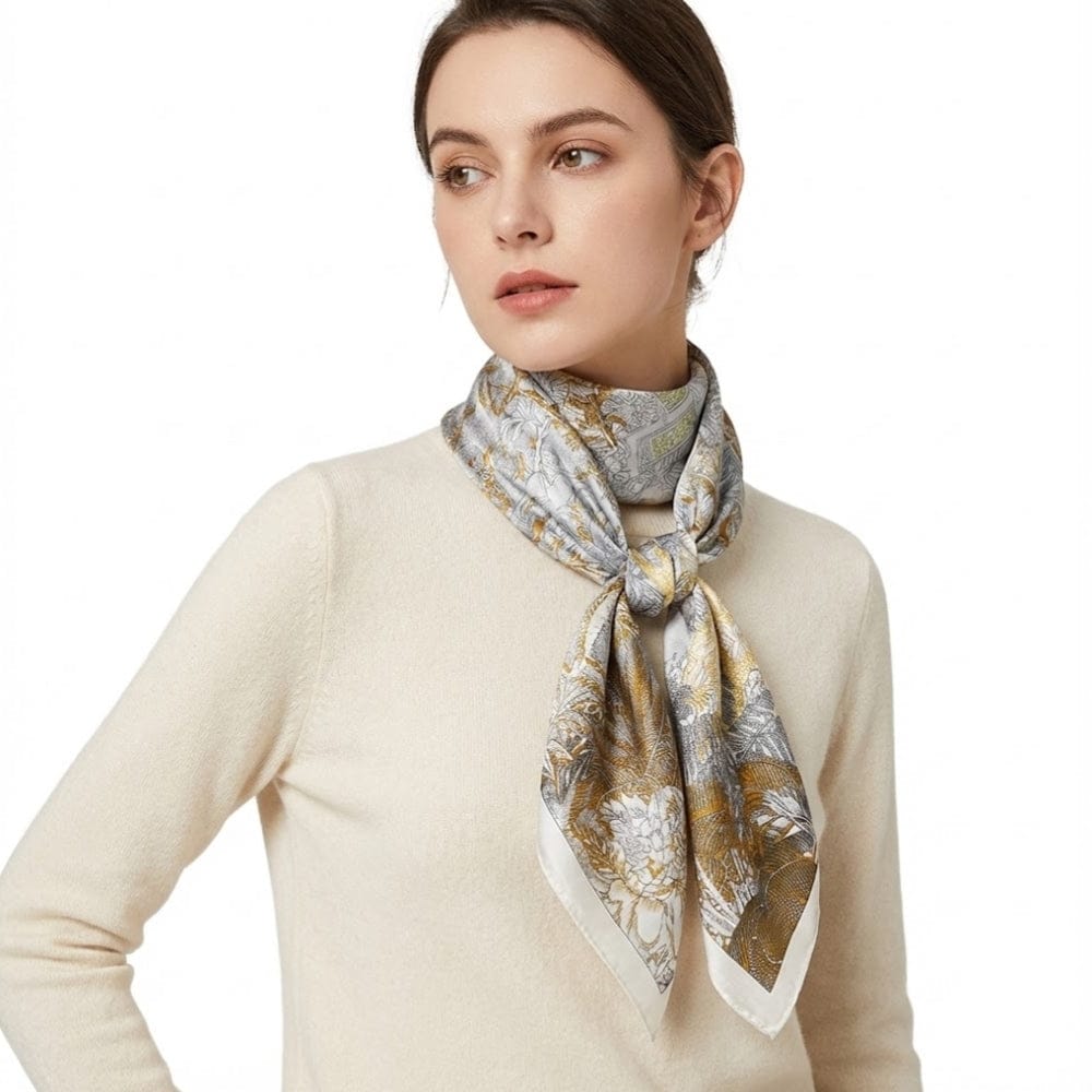 Foulard en soie noué autour du cou, motifs floraux dorés et argentés sur fond gris, porté par une femme