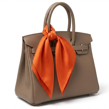 Foulard en soie orange noué sur un sac à main beige, ajoutant une touche élégante et colorée à l'ensemble
