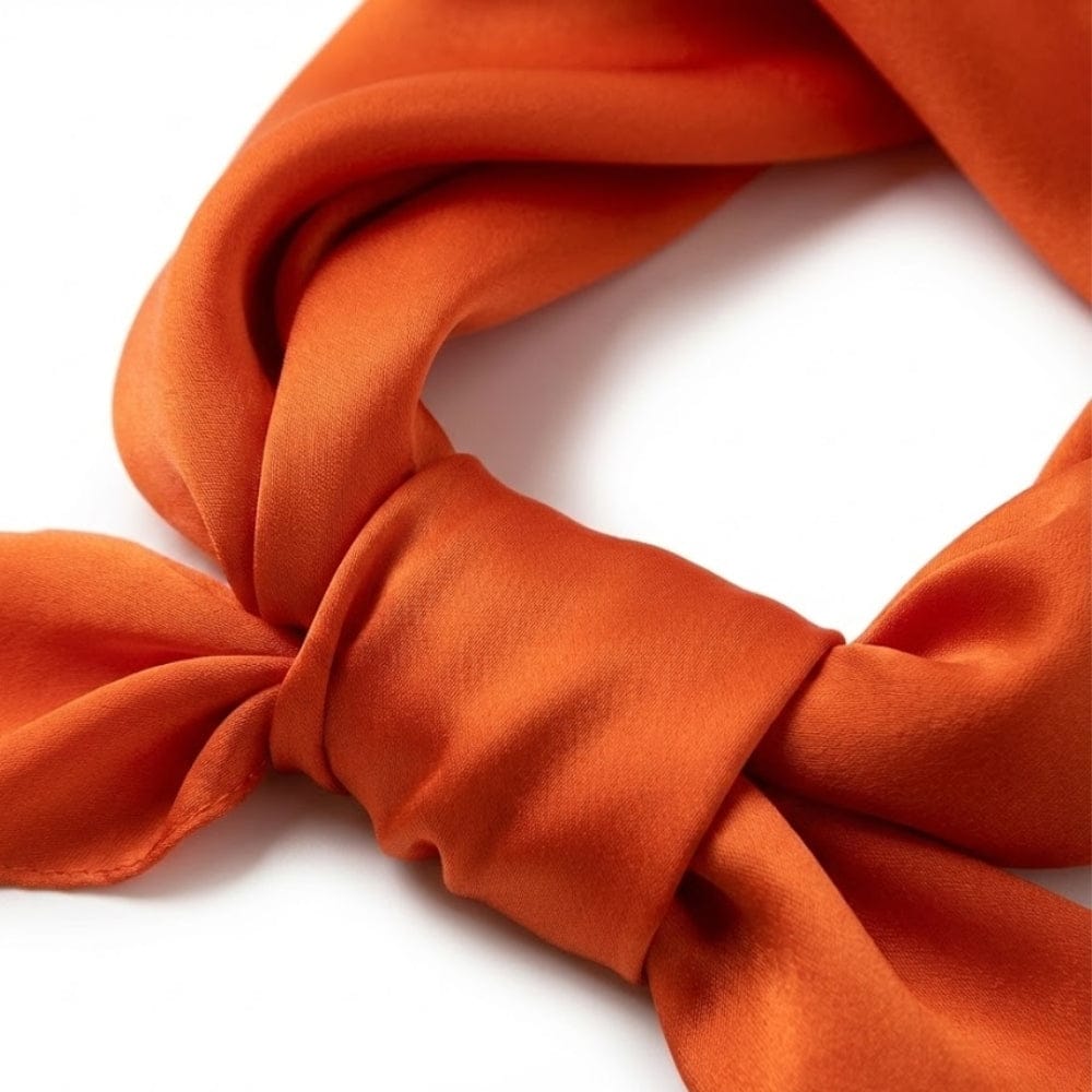 Foulard en soie orange noué, avec une texture lisse et brillante, mettant en valeur une élégance raffinée