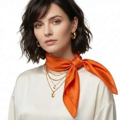 Foulard en soie orange noué autour du cou d'une femme, avec un haut beige et des bijoux dorés