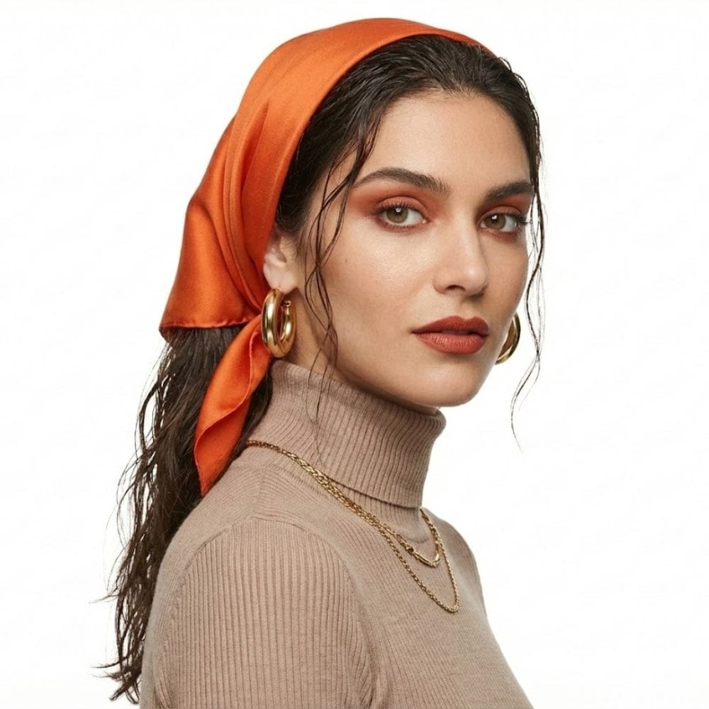 Foulard en soie orange noué sur une femme au teint lumineux, avec un haut beige et des boucles d'oreilles dorées