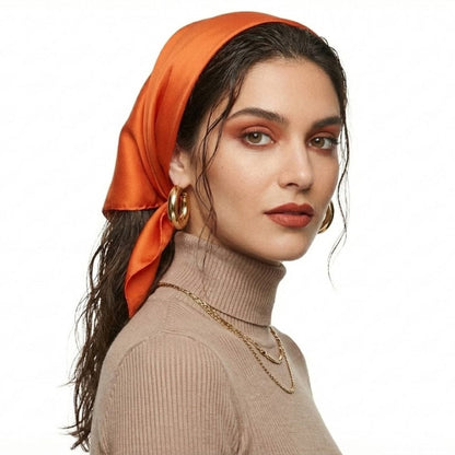 Foulard en soie orange noué sur une femme au teint lumineux, avec un haut beige et des boucles d'oreilles dorées