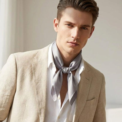 Foulard en soie gris noué autour du cou d'un homme, porté avec un blazer beige dans un décor lumineux