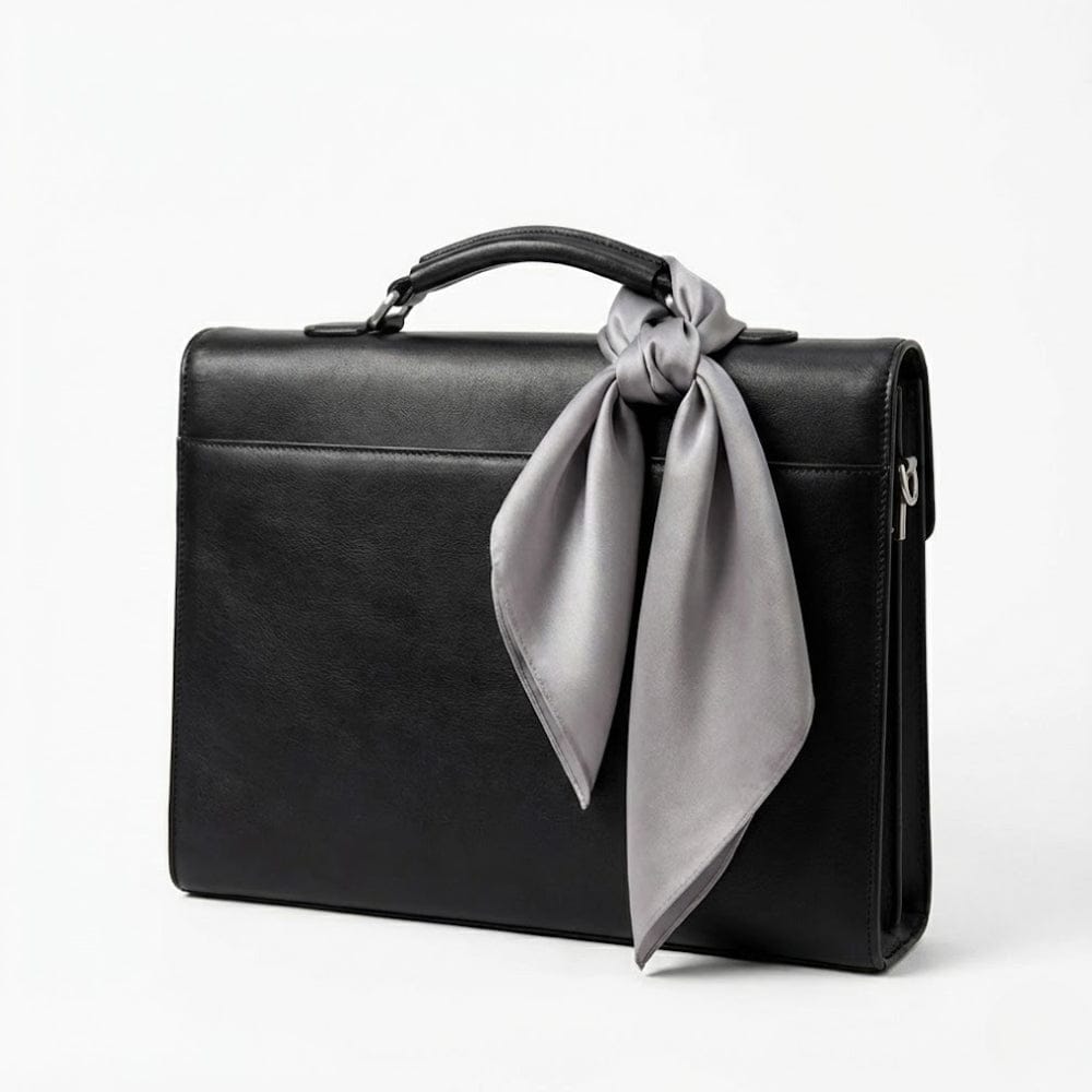 Foulard en soie gris noué sur une mallette noire, ajoutant une touche d'élégance discrète à l'ensemble