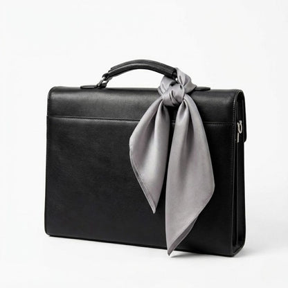 Foulard en soie gris noué sur une mallette noire, ajoutant une touche d'élégance discrète à l'ensemble
