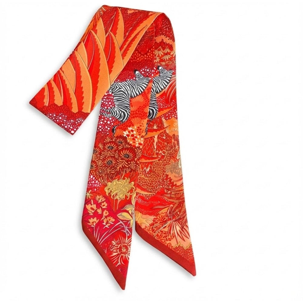 Foulard en satin aux motifs floraux et animaliers, dominé par des teintes rouges et oranges, drapé élégamment
