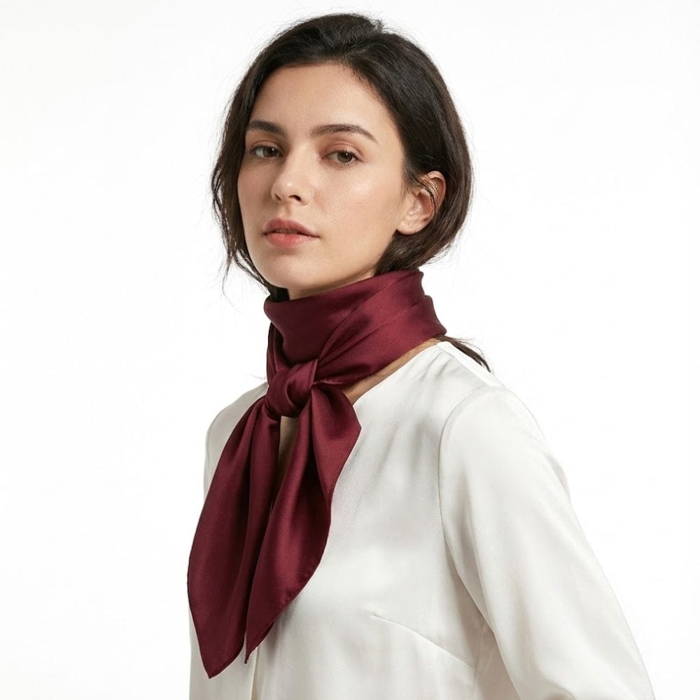 Foulard en satin bordeaux noué autour du cou, porté par une femme en blouse blanche sur fond blanc