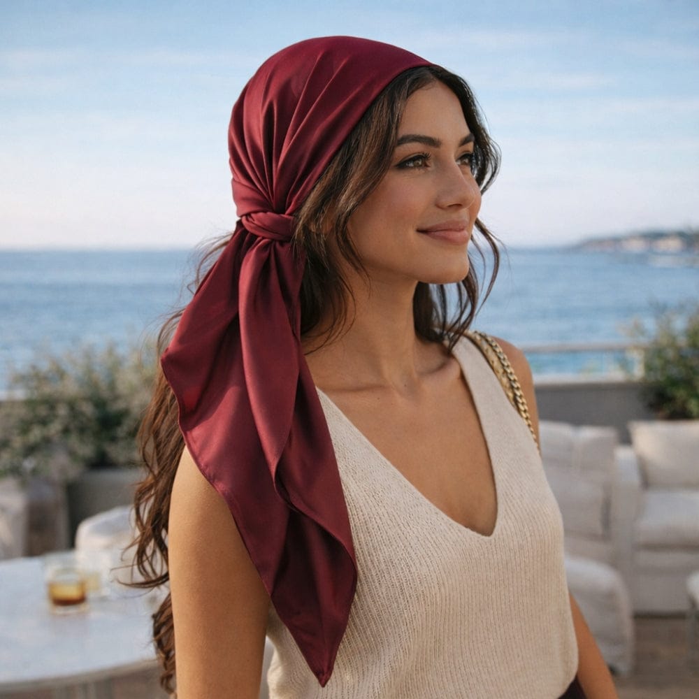 Foulard en satin rouge noué, porté par une femme au bord de la mer, avec un style élégant et intemporel