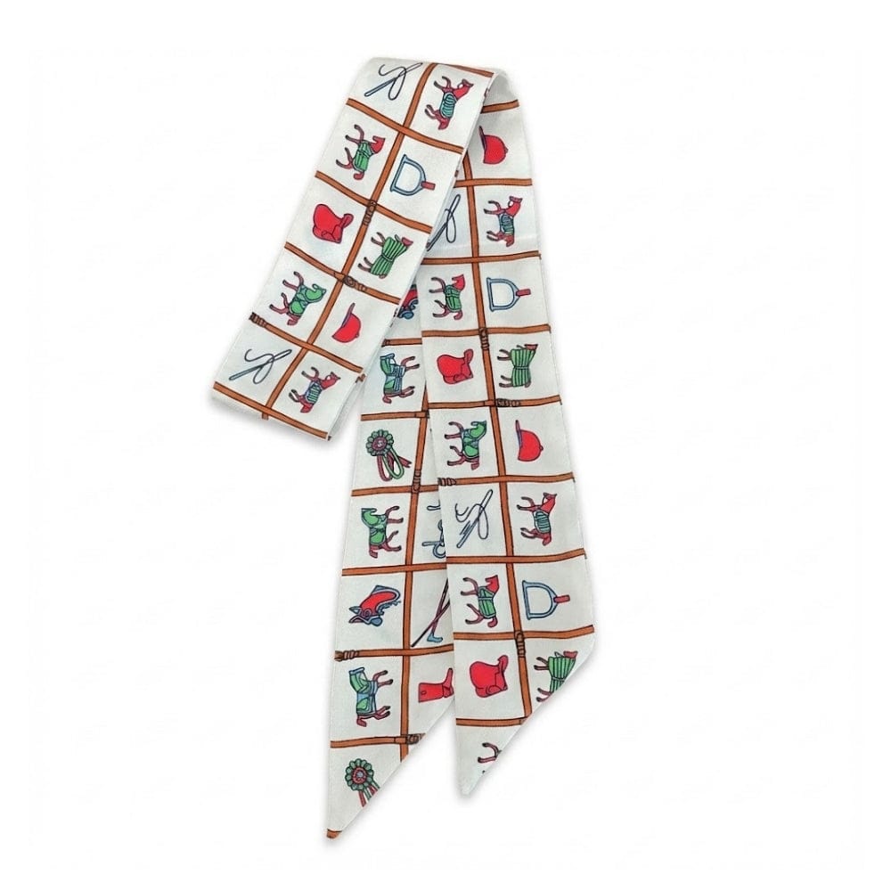 Foulard en soie blanc avec motifs colorés de ciseaux et accessoires, noué élégamment sur un sac à main