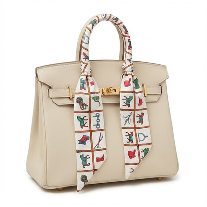 Foulard en soie noué sur un sac à main beige, avec motifs colorés de dessins ludiques et élégants