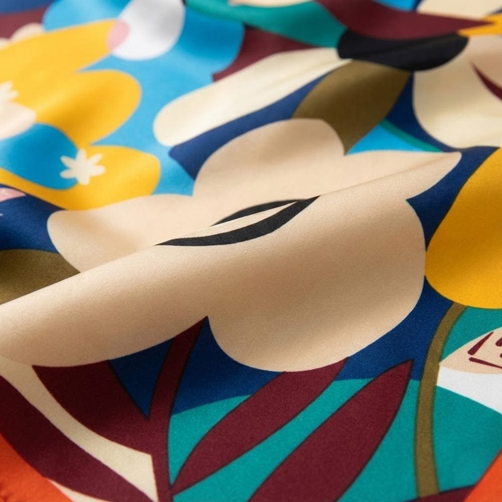 Foulard en satin aux motifs floraux colorés, présentant des teintes de bleu, jaune et rouge sur fond beige