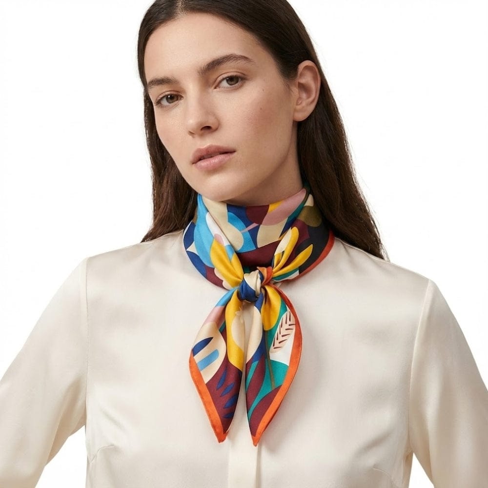 Foulard en satin coloré noué autour du cou, avec des motifs géométriques sur fond sombre, porté par une femme