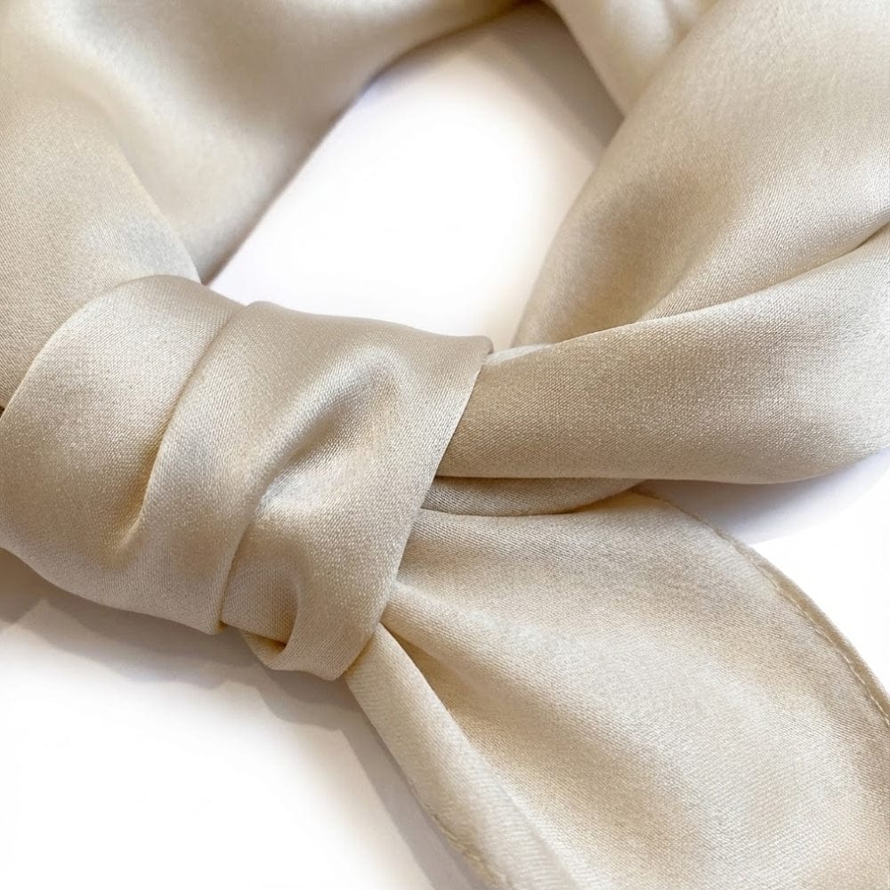 Foulard en soie beige noué, avec une texture lisse et brillante, sur fond blanc