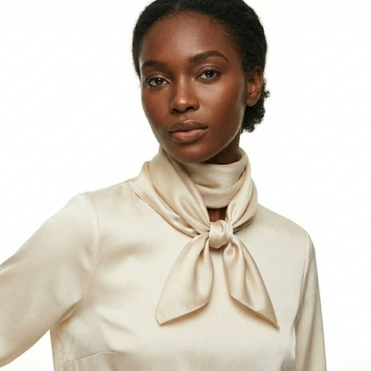 Foulard en satin beige noué autour du cou d'une femme, mettant en valeur l'élégance et la douceur de la matière