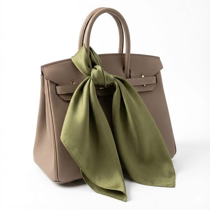 Foulard en soie vert noué sur une élégante sacoche beige, mettant en valeur sa douceur et sa brillance