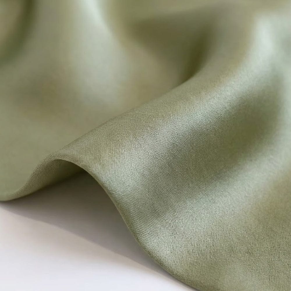Foulard en soie vert aux teintes raffinées, présentant une texture douce et lumineuse, légèrement ondulé sur une surface blanche