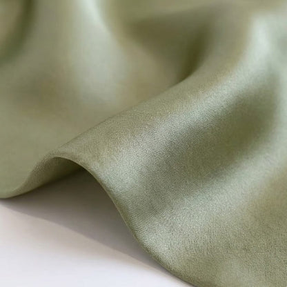 Foulard en soie vert aux teintes raffinées, présentant une texture douce et lumineuse, légèrement ondulé sur une surface blanche