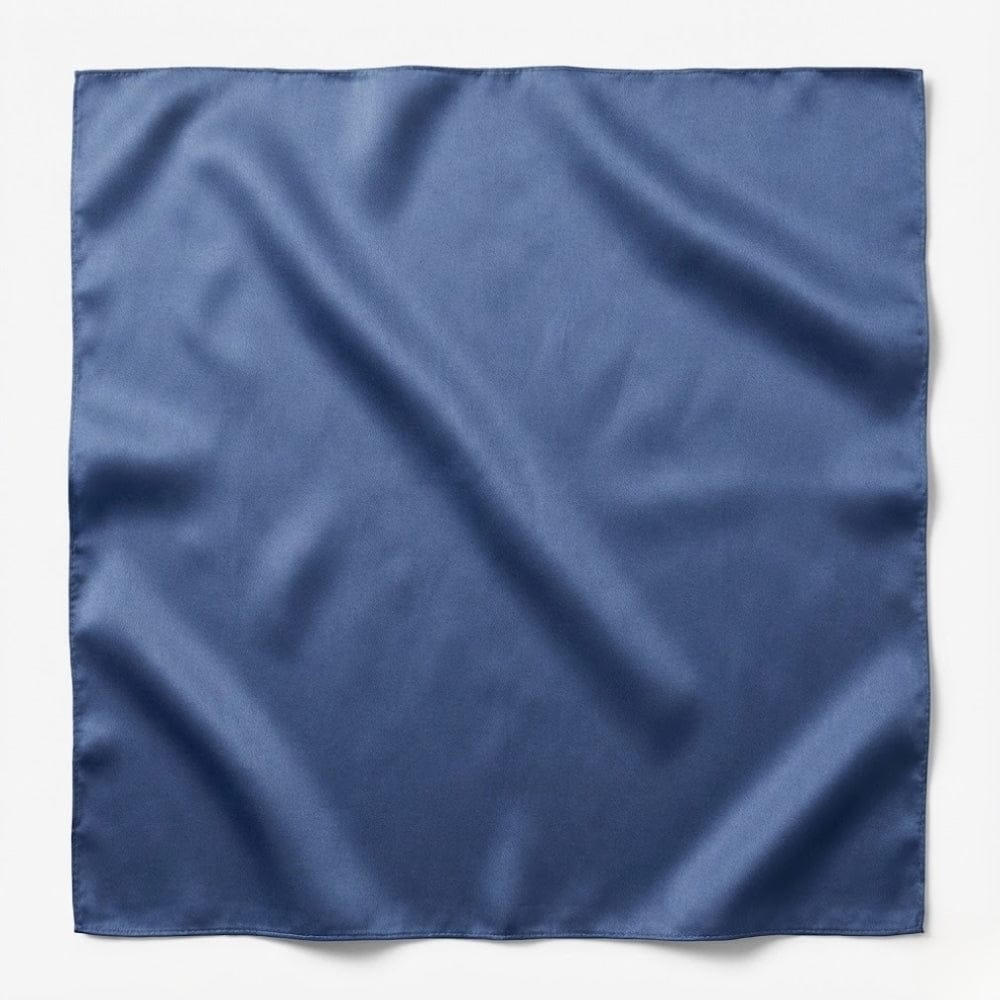 Foulard carré en soie bleu, brillant et lisse, posé sur une surface blanche, mettant en valeur sa texture raffinée