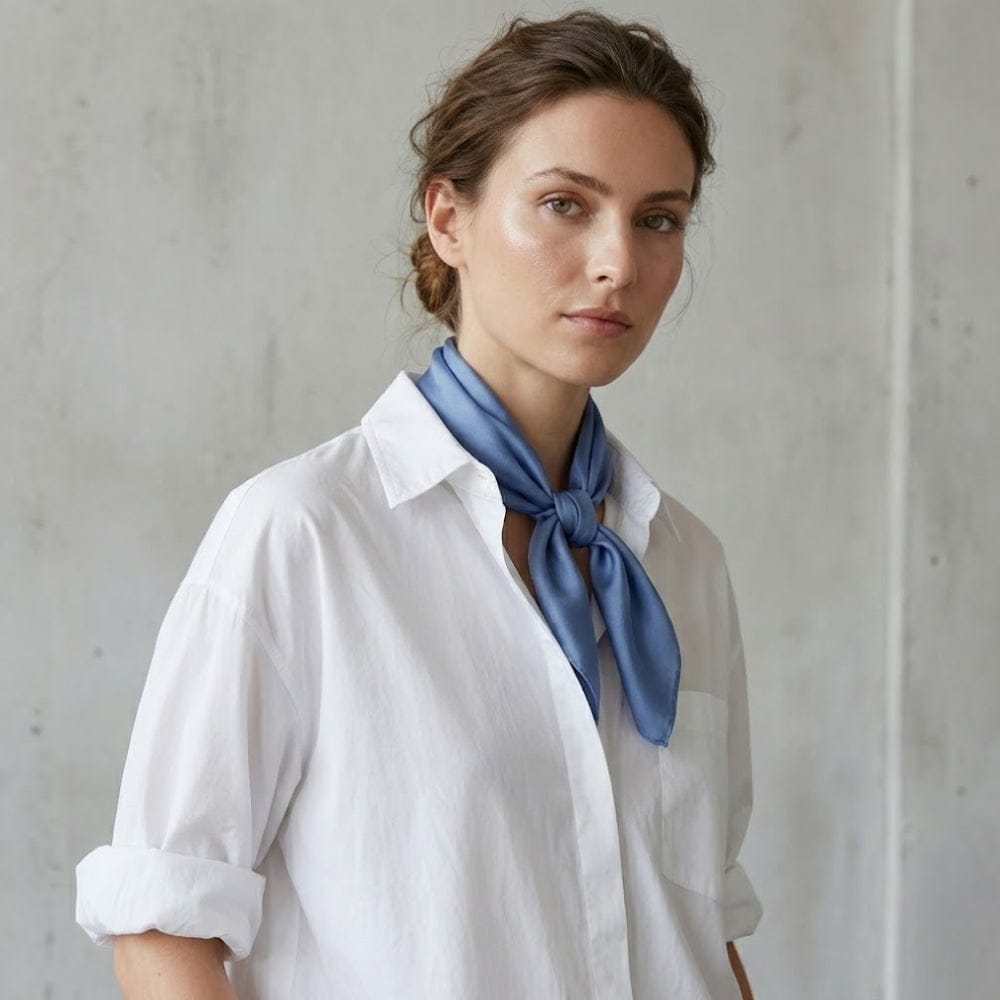 Foulard en soie bleu noué autour du cou d'une femme, avec une brillance soyeuse sur fond neutre