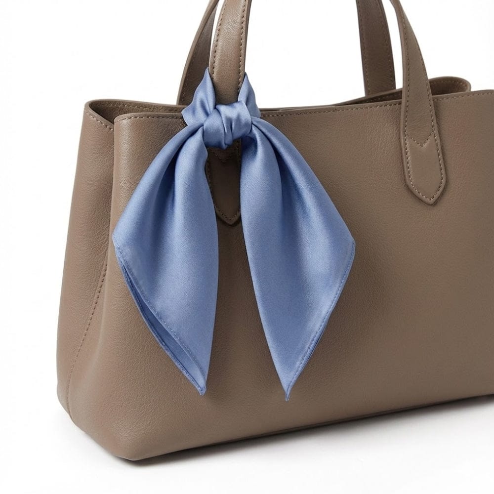 Foulard en soie bleu noué sur une anse de sac en cuir beige, ajoutant une touche élégante et raffinée